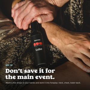 Hands holding a bottle of BUM Silicone Lube on a fur blanket, with a tip to use it during foreplay