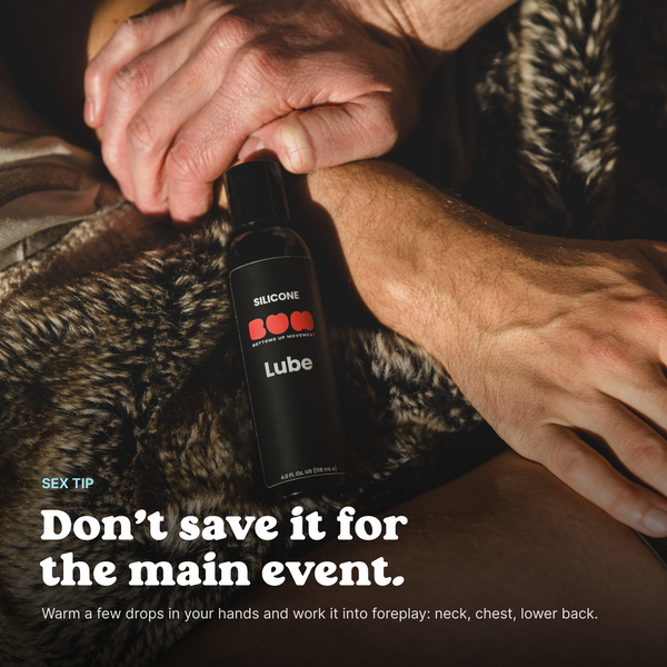 Hands holding a bottle of BUM Silicone Lube on a fur blanket, with a tip to use it during foreplay